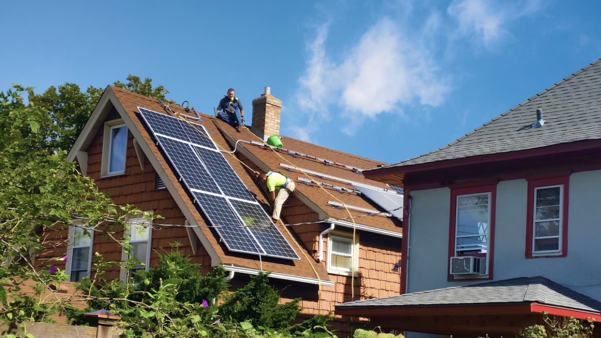 Image of suburban house with solar panels in fron of brigh blue sky.